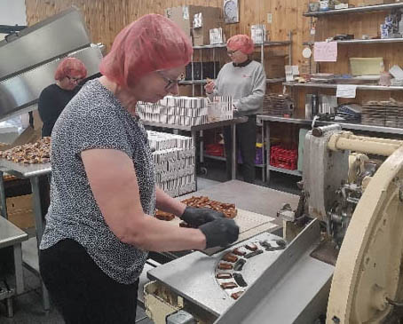 A Dutch House Caramels employee feeds caramels into a wrapping machine.  Behind her are two women packing the wrapped caramels into boxes to ship to their customers.