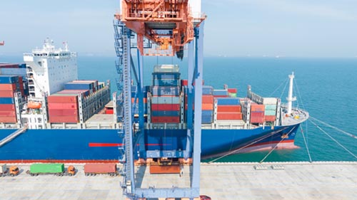 Crane loading a cargo container from truck to container ship